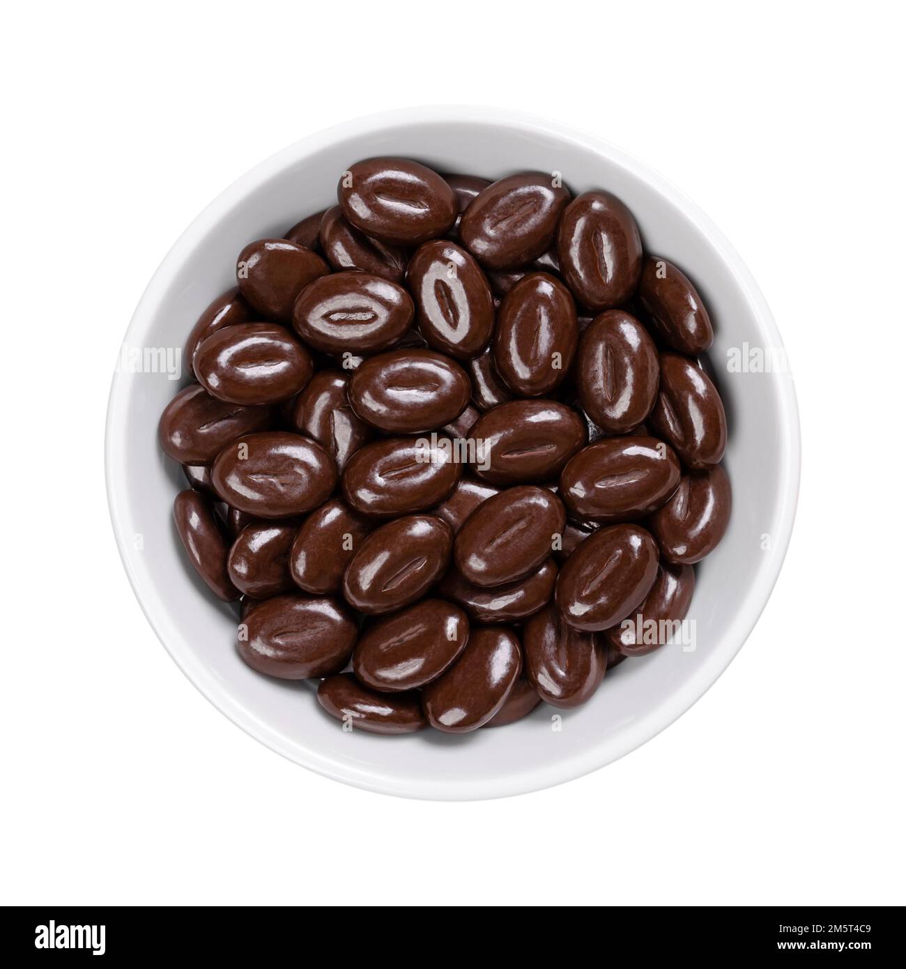 Chicchi di moka al cioccolato fondente, in un recipiente bianco. Caramelle fatte di una miscela di sapore di caffè in grani con indulgente cioccolato fondente, a forma di caffè in grani. Foto Stock