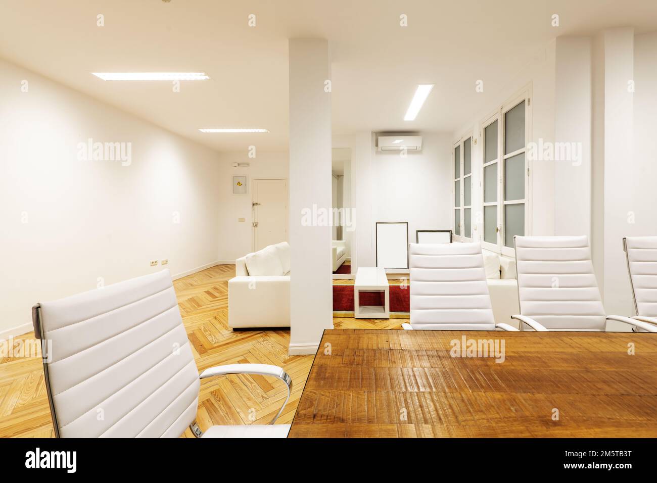Ufficio con tavolo da conferenza in legno grezzo, sedie girevoli rivestite bianche e divani coordinati Foto Stock