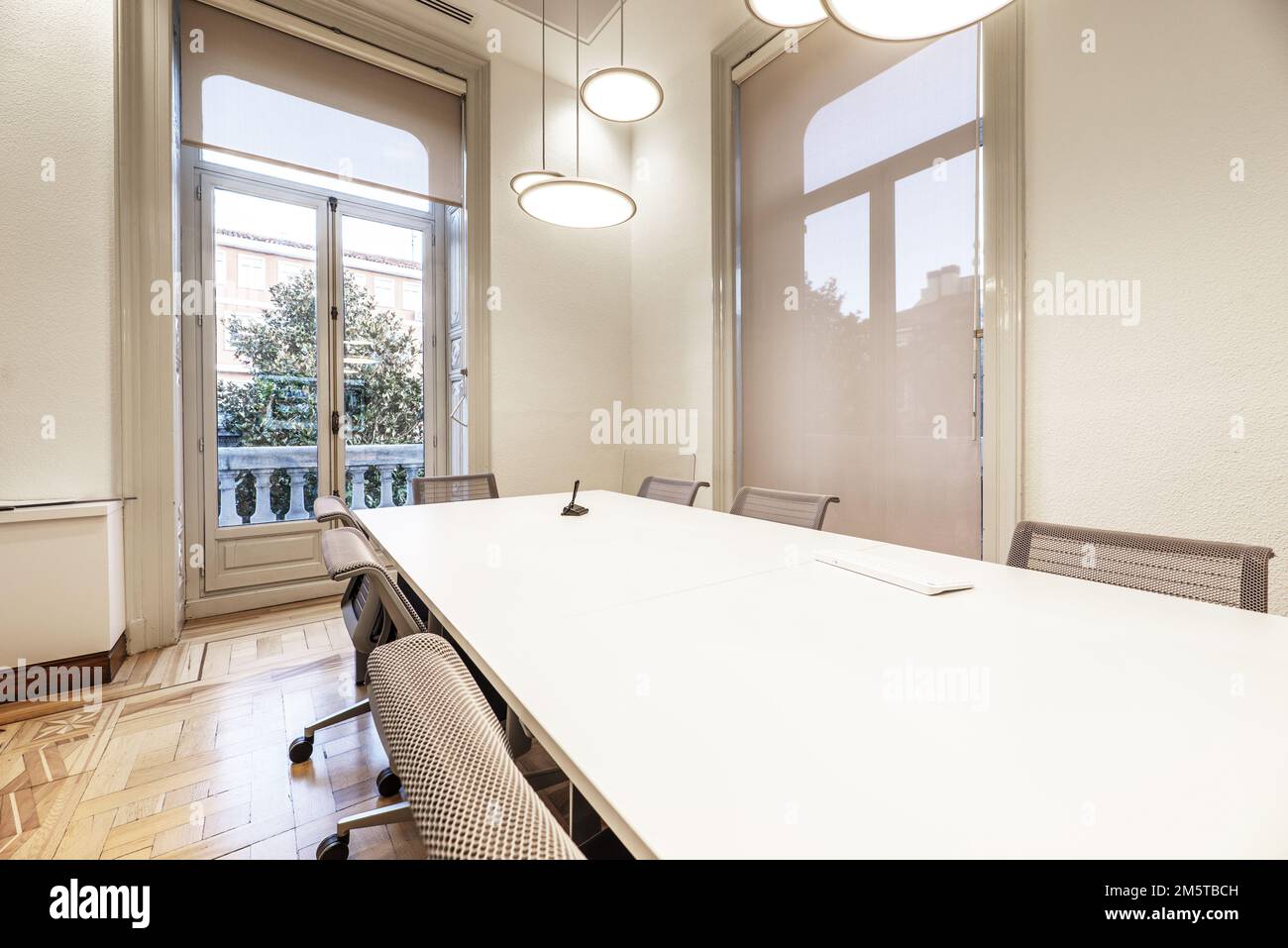 Sala consiliare di un imponente edificio d'epoca con lungo tavolo di legno bianco con sedie girevoli grigie Foto Stock