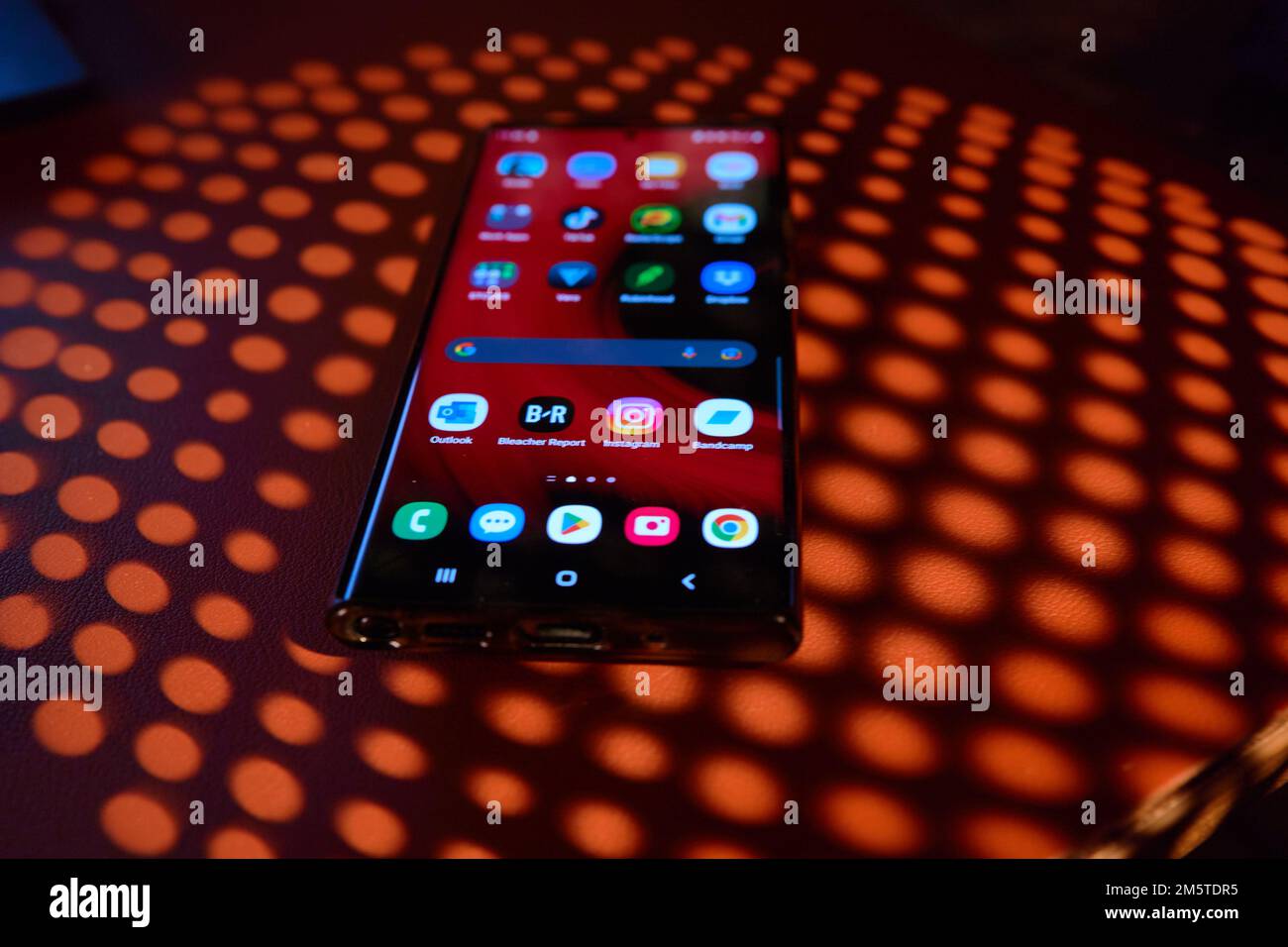 Telefono cellulare con applicazioni luminose visualizzate sull'ombra del tavolo Foto Stock
