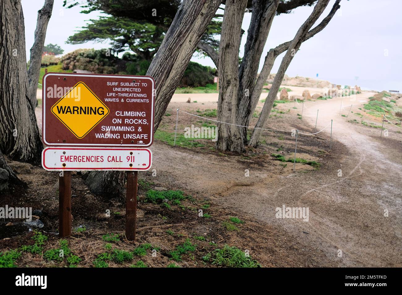 Cartello vicino a Lucas Point a Pacific Grove, California, USA; avviso ai visitatori di pericolose condizioni della spiaggia e dell'oceano; pericolo di vita onde, correnti. Foto Stock