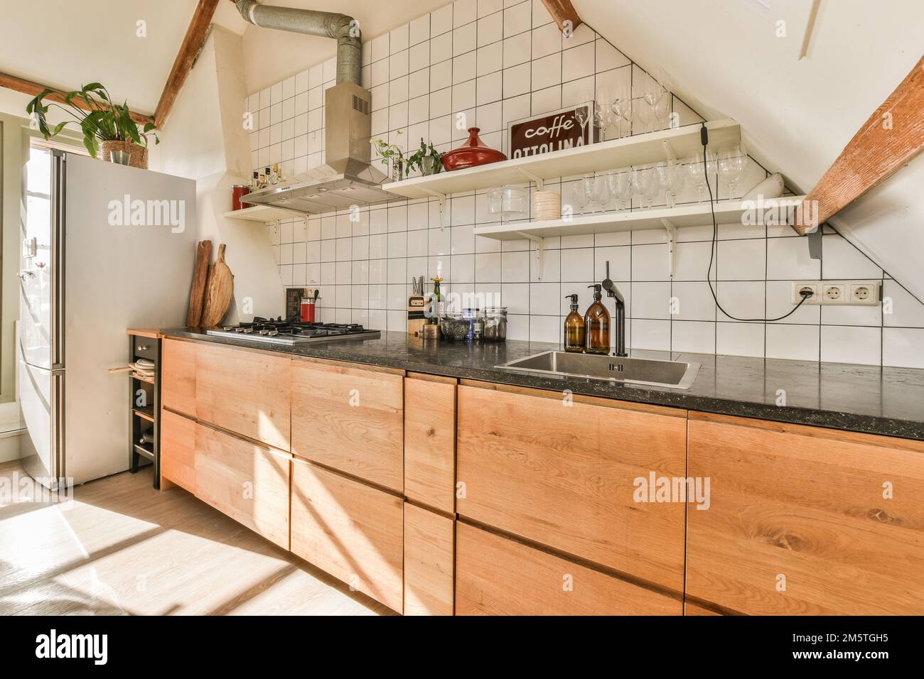 una cucina con armadi in legno e ripiani neri al centro della stanza è una porta aperta che conduce ad un piccolo patio Foto Stock