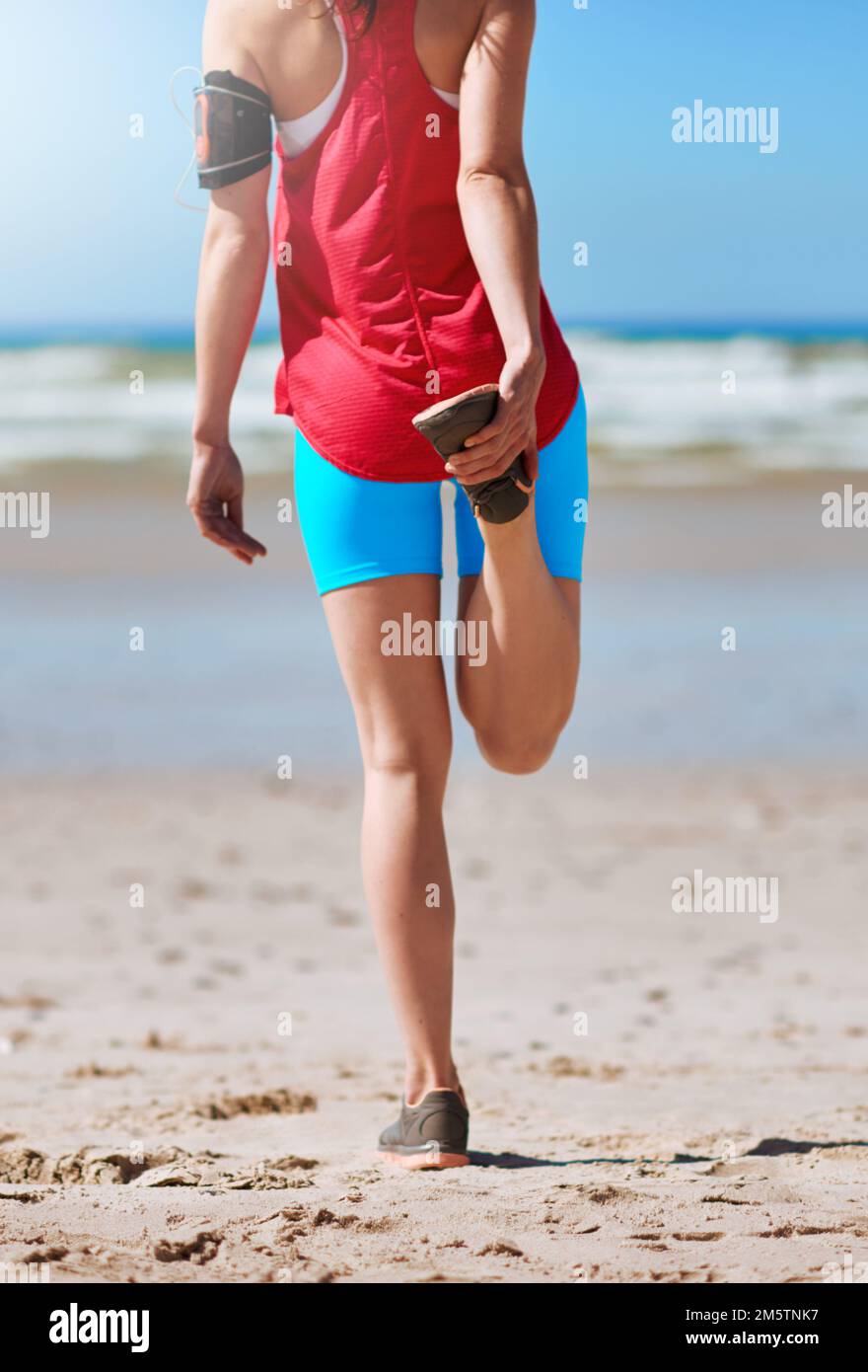 Allungamento per evitare lesioni. Ripresa retroversa di una giovane donna che si allunga prima della sua corsa sulla spiaggia. Foto Stock