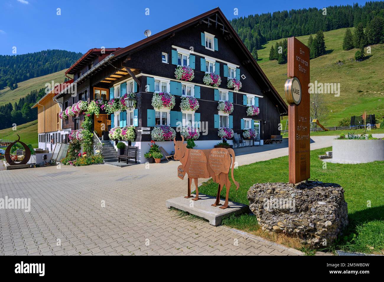 Alpe Berg agriturismo con esuberanti decorazioni floreali e pannello di informazioni sulle mucche di ferro nella valle di Balderschwanger, Allgaeu, Baviera, Germania Foto Stock