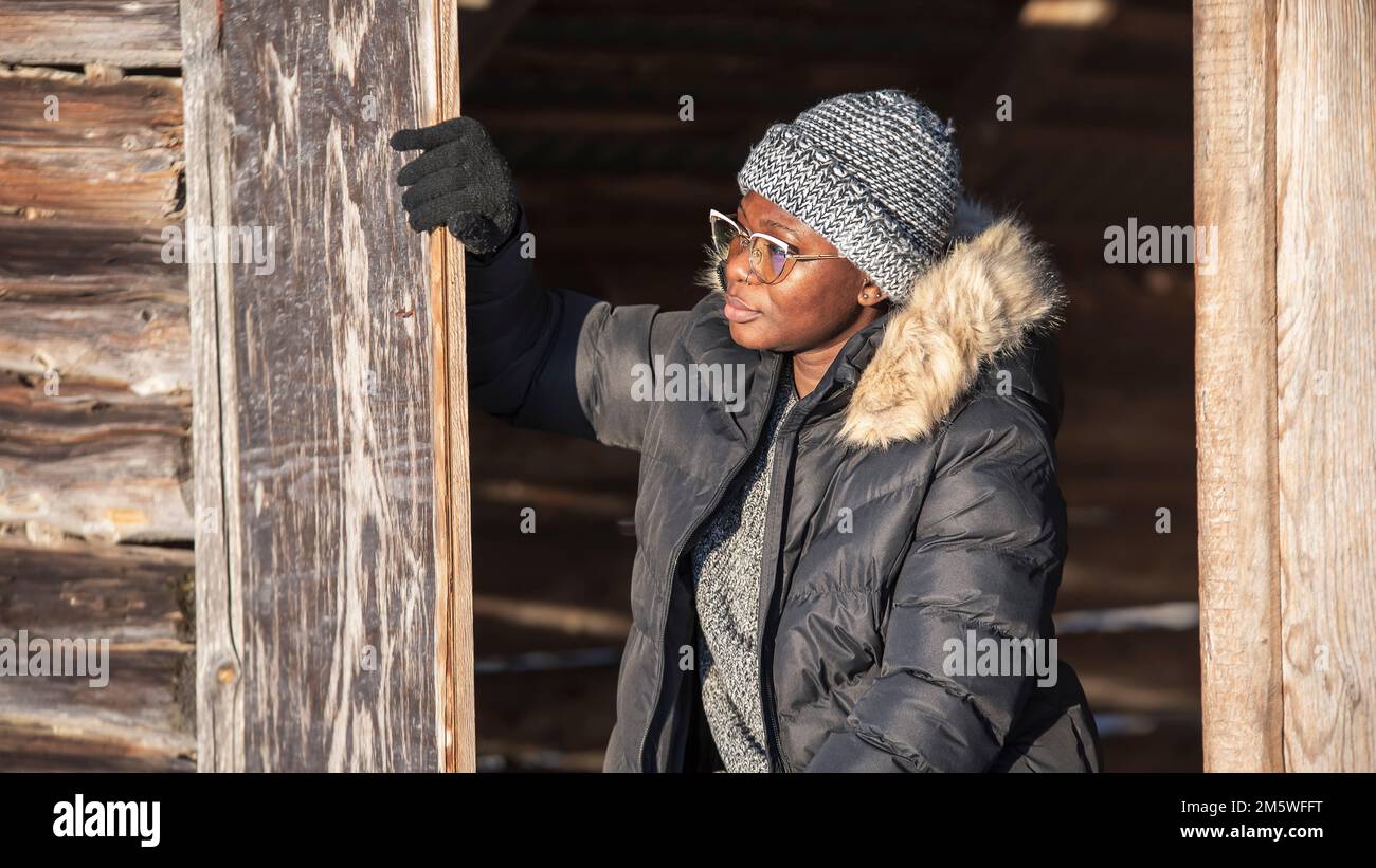 Donna africana seduta in una porta in un fienile di campagna godendo il sole nel mese di inverno di dicembre Foto Stock