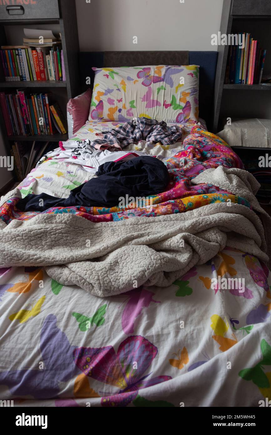 Camera da letto: Letto non fatto con biancheria da letto sgualcita accanto ad una libreria piena di libri. Foto Stock