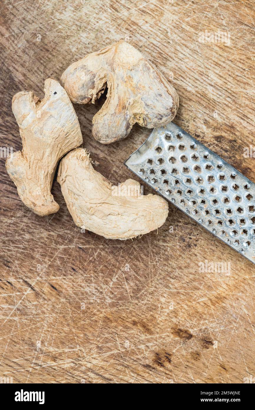 Pezzi di zenzero essiccati e grattugia metallica su una superficie rustica in legno. Preparazione degli ingredienti delle spezie Foto Stock