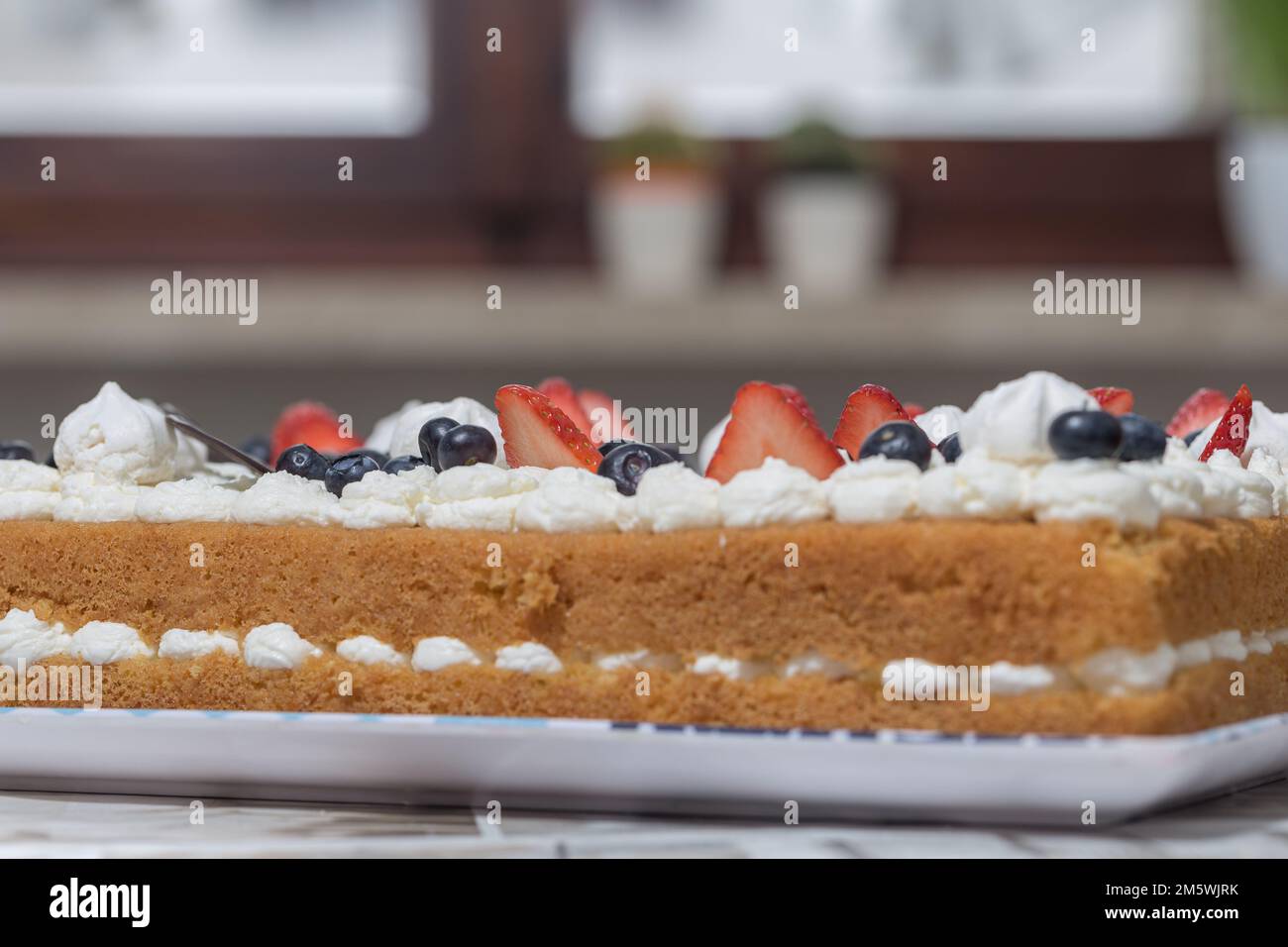 Primo piano di una deliziosa torta con panna, fragole e mirtilli. Appetitosa consistenza da dessert. Foto Stock