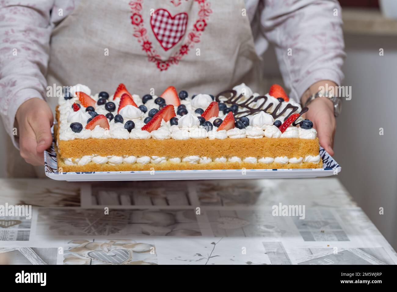 Mani che reggono una grande torta con panna, fragole, mirtilli. Festeggiamenti, servizio, dessert. Foto Stock