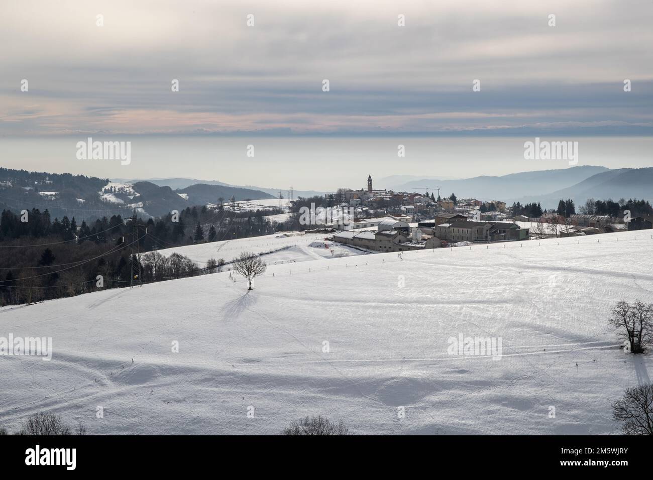Paesaggio invernale innevato con un villaggio incastonato tra colline sotto un cielo nuvoloso. Paesaggio rurale. Foto Stock
