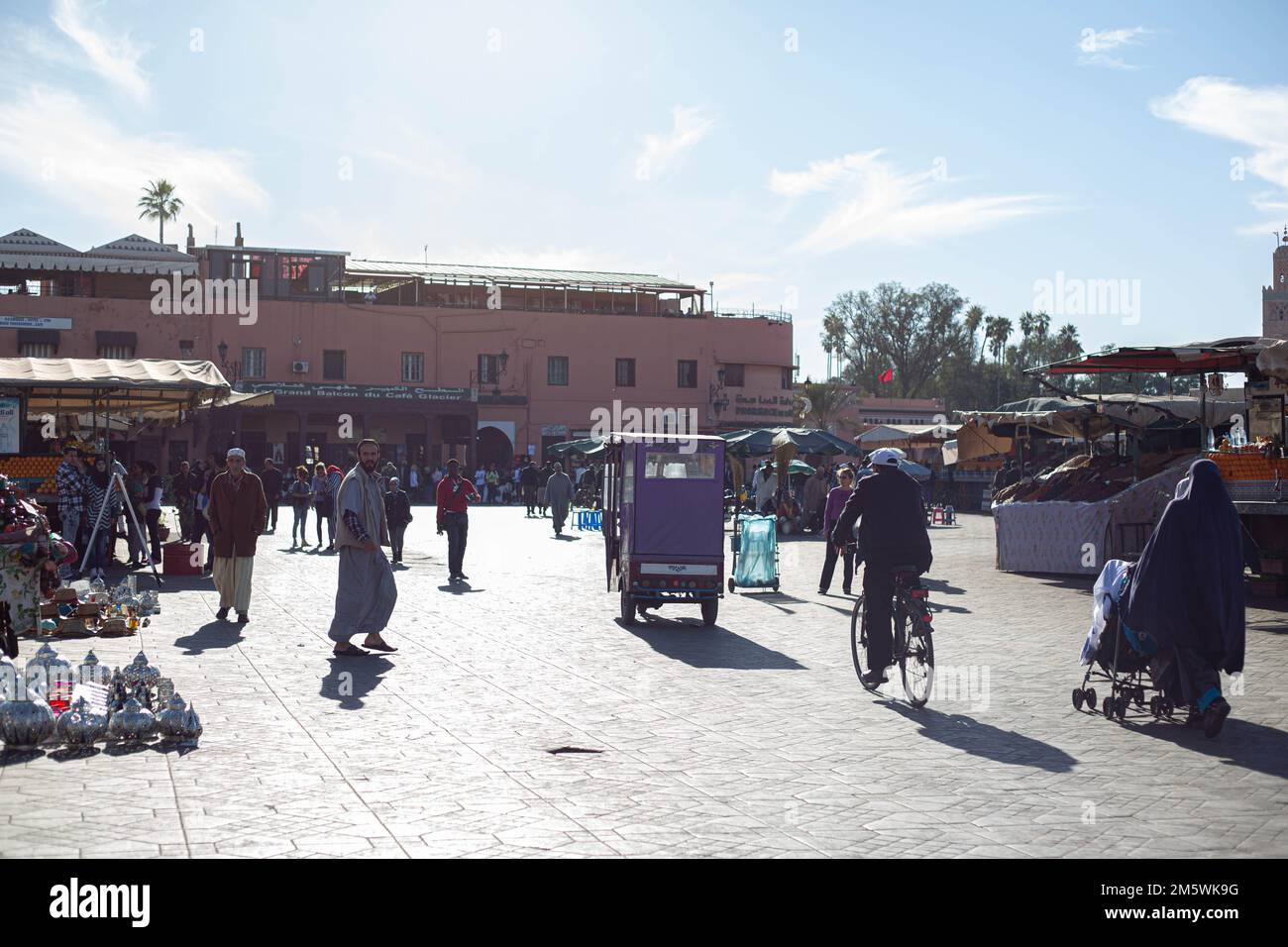 Soleggiata scena di strada a Marrakech, Marocco. Gente che cammina, carretti, palme, edifici. Vivace vita cittadina. Foto Stock