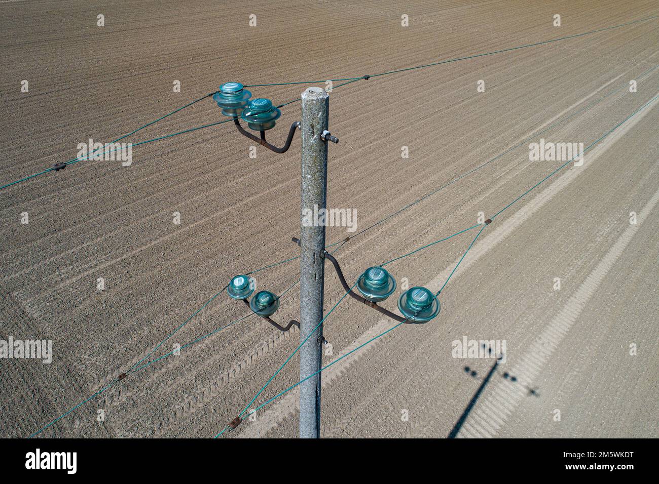 Ripresa aerea di un'asta di servizio con isolatori in vetro. Linee elettriche che attraversano un campo coltivato. Foto Stock