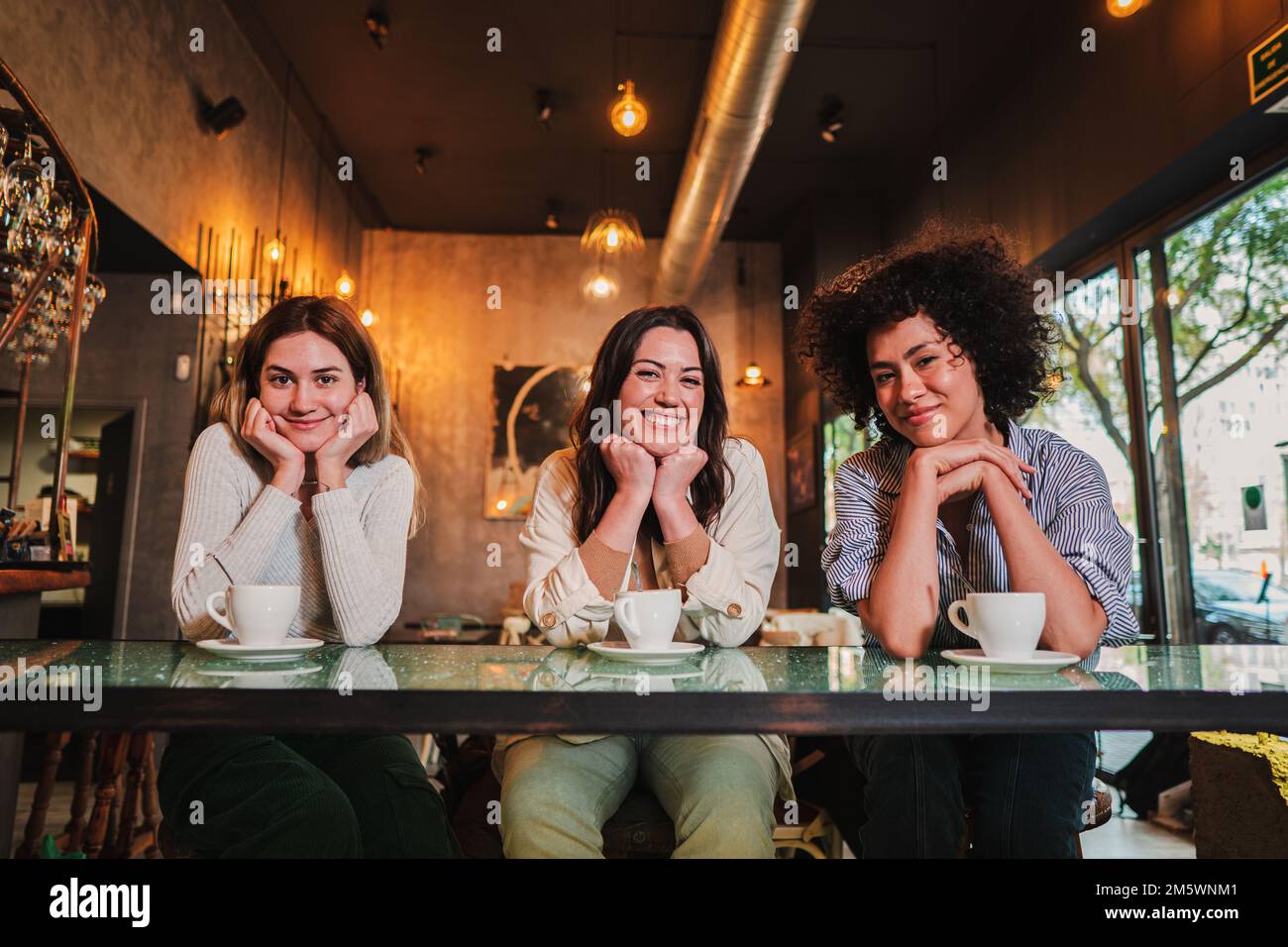 Ritratto di te giovani donne sorridenti e in posa guardando la macchina fotografica in un bar. Foto di un gruppo di donne felici in un ristorante o bar. Foto di alta qualità Foto Stock