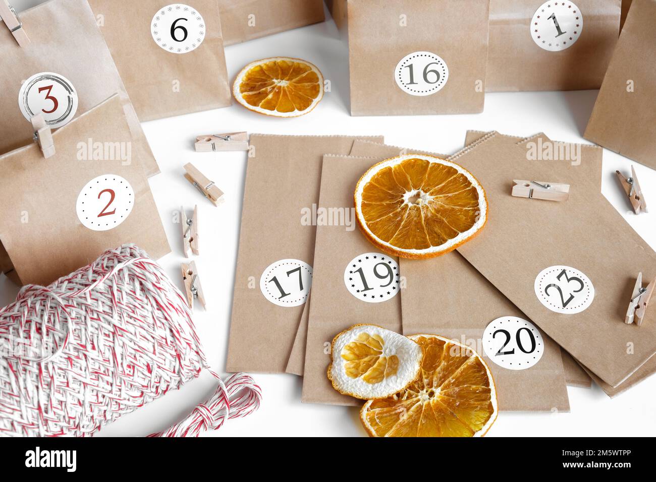 Calendario dell'Avvento di Natale. Sacchetti di carta, frutta secca, stringa su tavolo bianco. Attività stagionale per bambini, vacanze invernali in famiglia. Calandra colorata fatta a mano Foto Stock