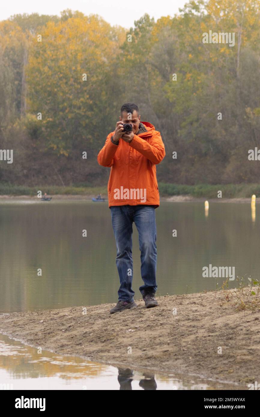 Ritratto di un viaggiatore al lago in autunno scattando una foto con la fotocamera digitale e la giacca arancione. Foto di alta qualità Foto Stock