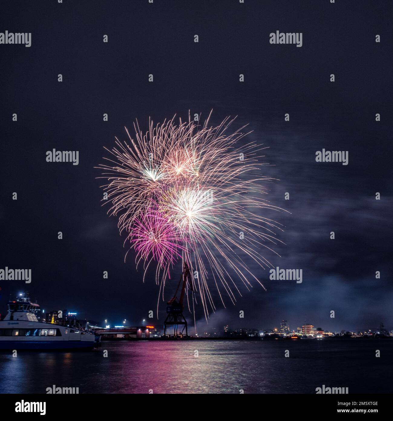 Fuochi d'artificio del nuovo anno a gothenburg svezia con vaporetto in primo piano e vecchie gru dai colori esplosivi Foto Stock