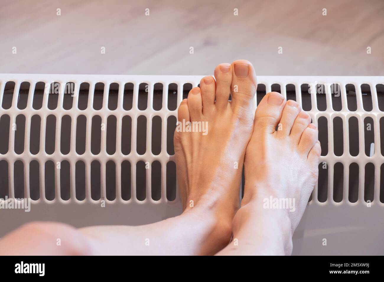 gambe femminili su una batteria a casa, stagione di riscaldamento, gambe calde su una batteria elettrica, gambe Foto Stock