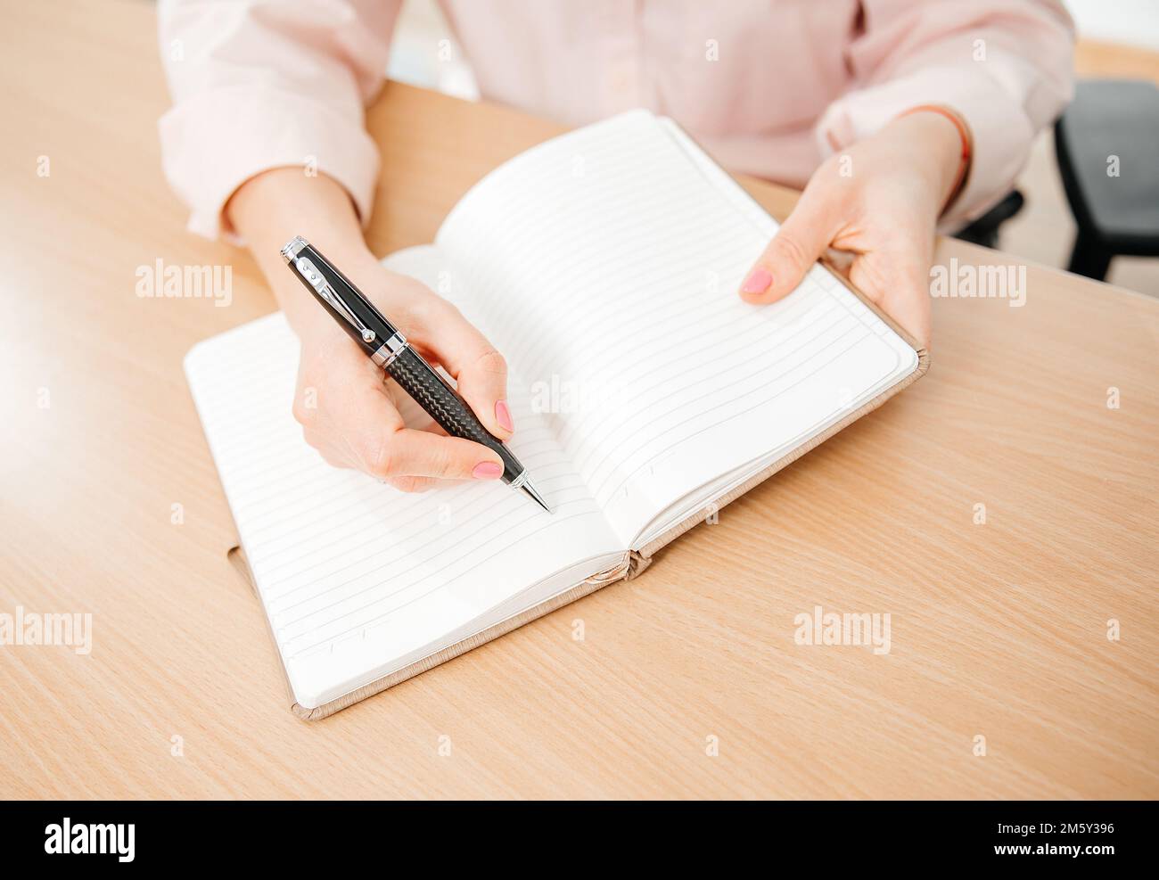 Primo piano delle mani di una donna che scrive in un blocco note posto su un tavolo di legno, ufficio domestico e concetto di lavoro, piani e previsioni Foto Stock