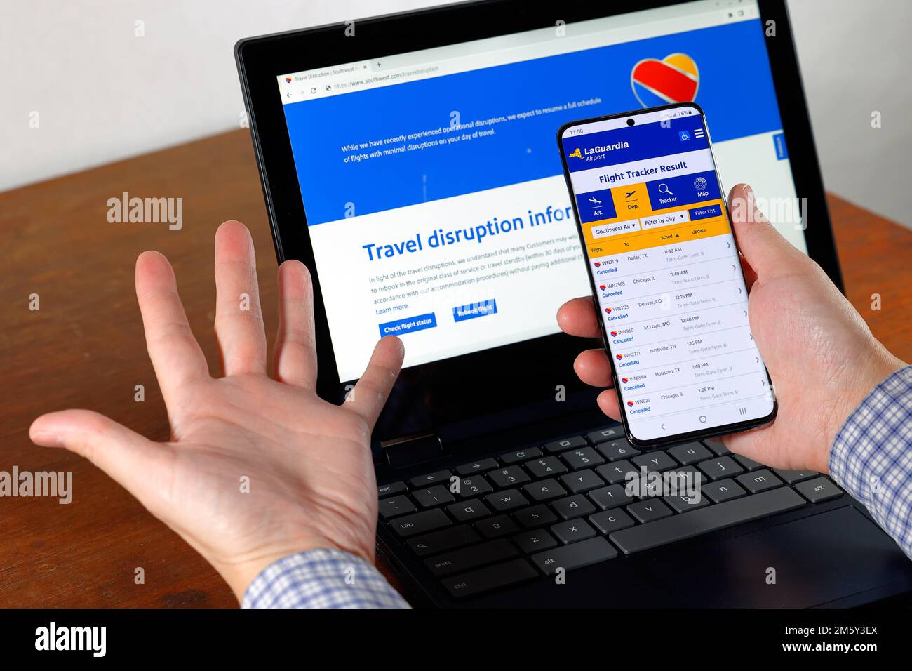 Le informazioni sulle cancellazioni dei voli e sulle interruzioni del viaggio di Southwest Airlines vengono visualizzate sullo smartphone e sullo schermo del computer con le mani in alto. Foto Stock