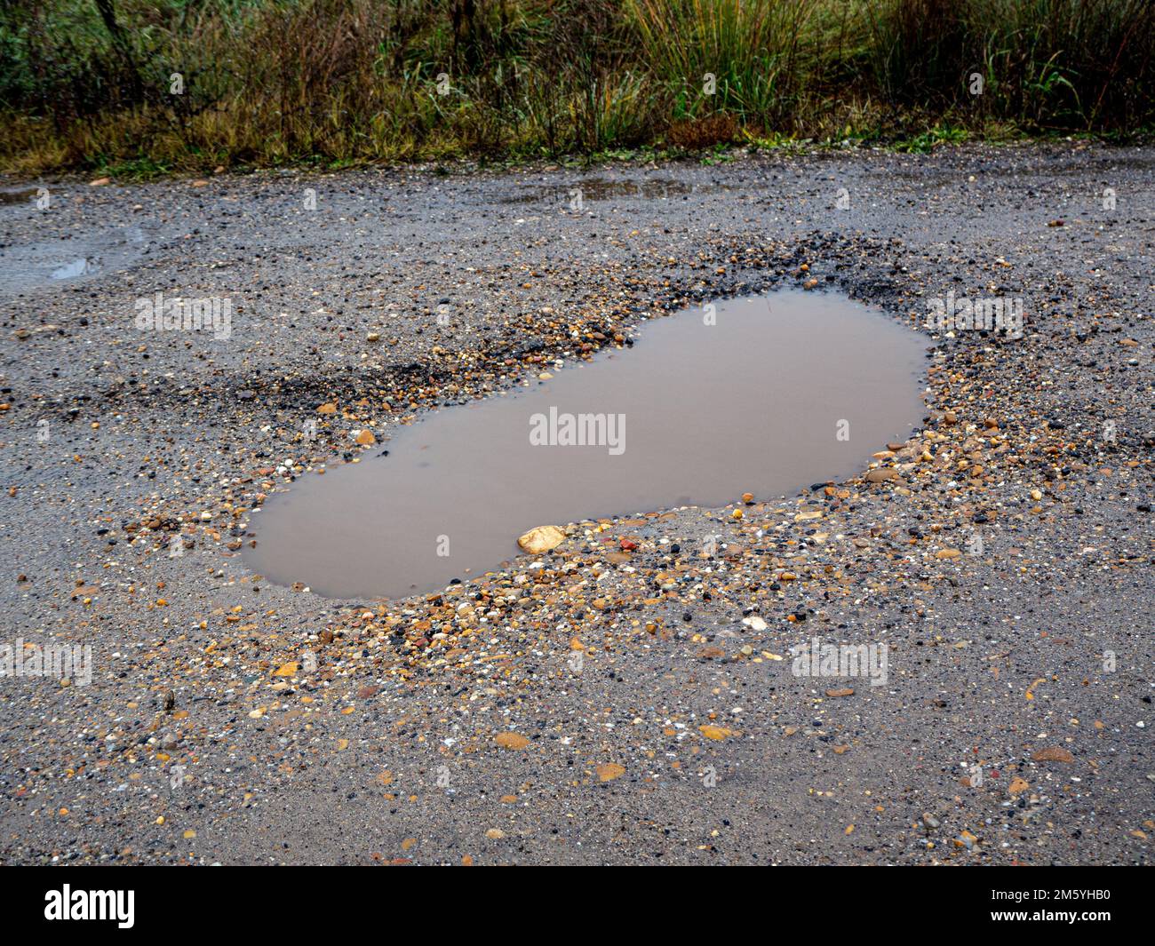 Pothole su una strada asfaltata in una giornata invernale piovosa. Concetto di rischio e problemi di traffico Foto Stock