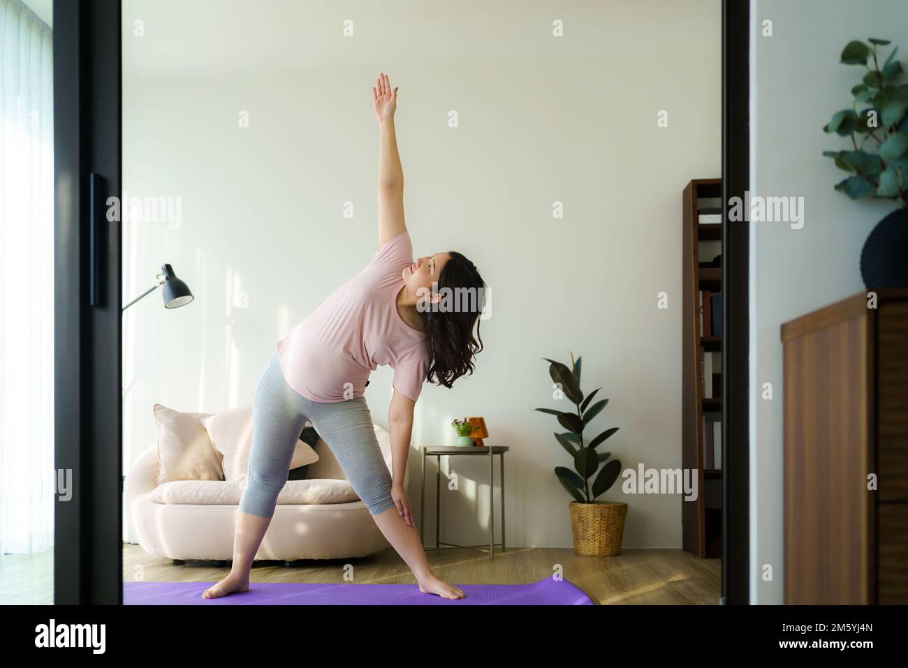 Intera lunghezza sana 6 mesi incinta calma donna asiatica meditare o fare esercizio di yoga a casa. Relax e stretching. Foto Stock