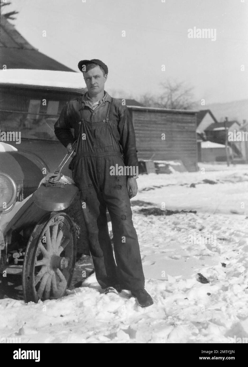 Un uomo con una chiave a mezzaluna molto grande si trova accanto ad un'auto legata alla neve che sta riparando, ca. 1930. Foto Stock