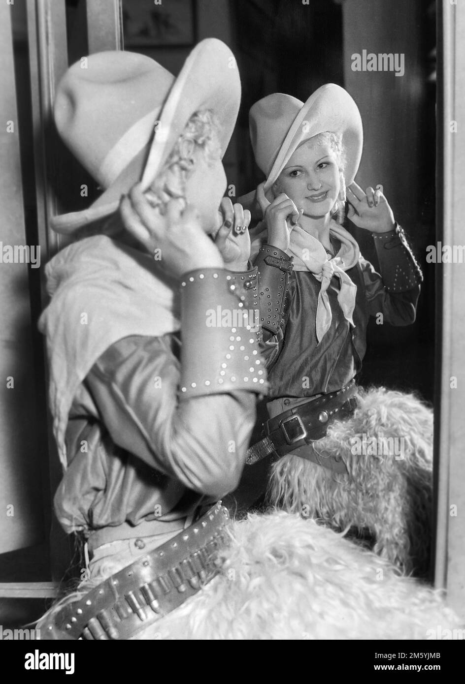 Una cowgirl bionda controlla le sue immagini in uno specchio per una foto promozionale per un rodeo nella California meridionale, ca. 1950. Foto Stock