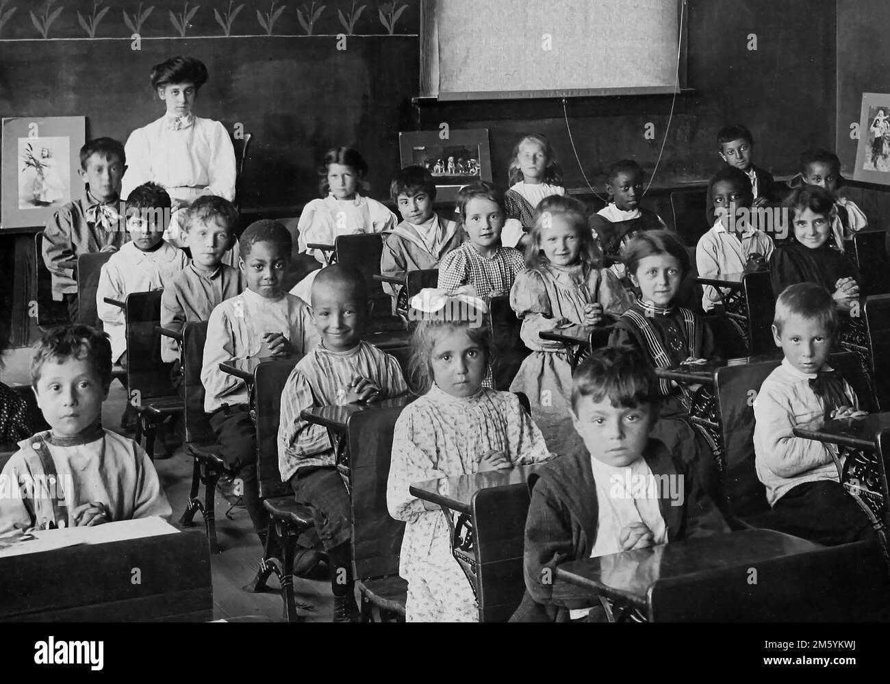 I bambini della scuola elementare si siedono alle loro scrivanie per una foto di classe, ca. 1910. Foto Stock