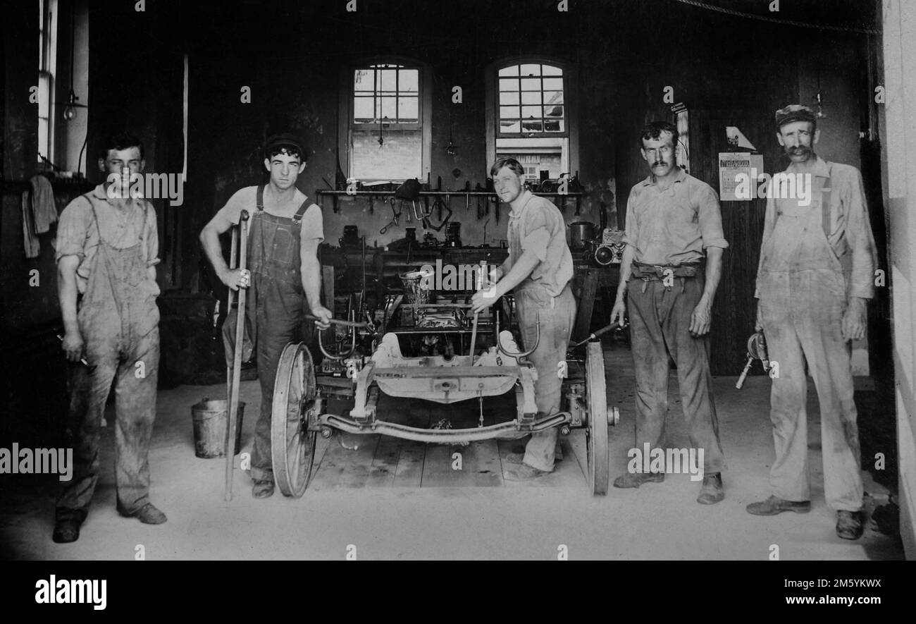 Meccanici in un garage auto pausa dal loro lavoro su una macchina, ca. 1922. Foto Stock