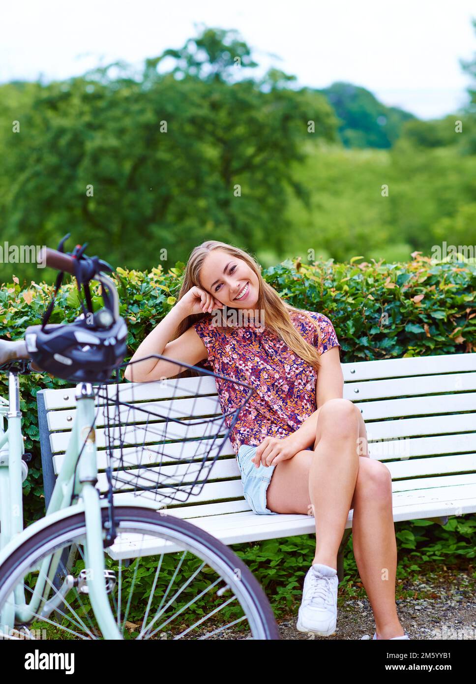 Che cosa sarebbe il fine settimana senza un giro piacevole fuori. una giovane donna seduta su una panchina mentre fuori per una bicicletta nel parco. Foto Stock