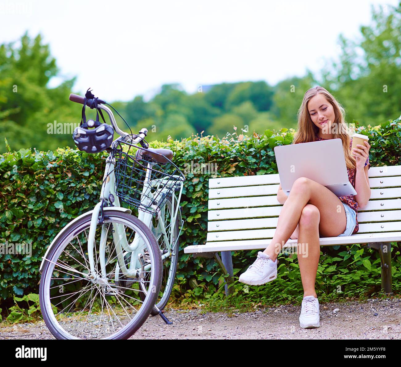 Libera di navigare ovunque si trovi. una giovane donna che usa un computer portatile su una panchina mentre fuori per una bicicletta nel parco. Foto Stock