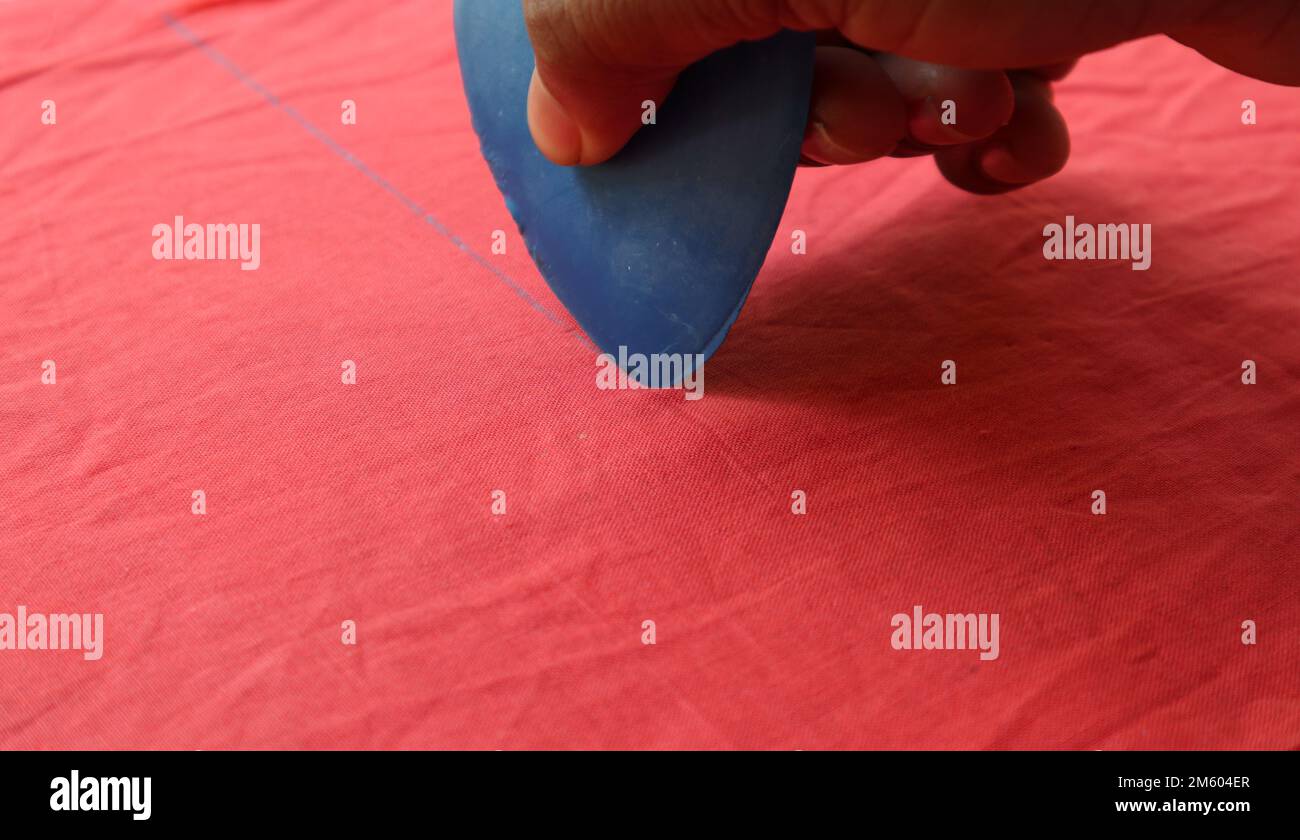 Una mano con il gesso blu del triangolo per disegnare la marcatura su un panno rosso Foto Stock