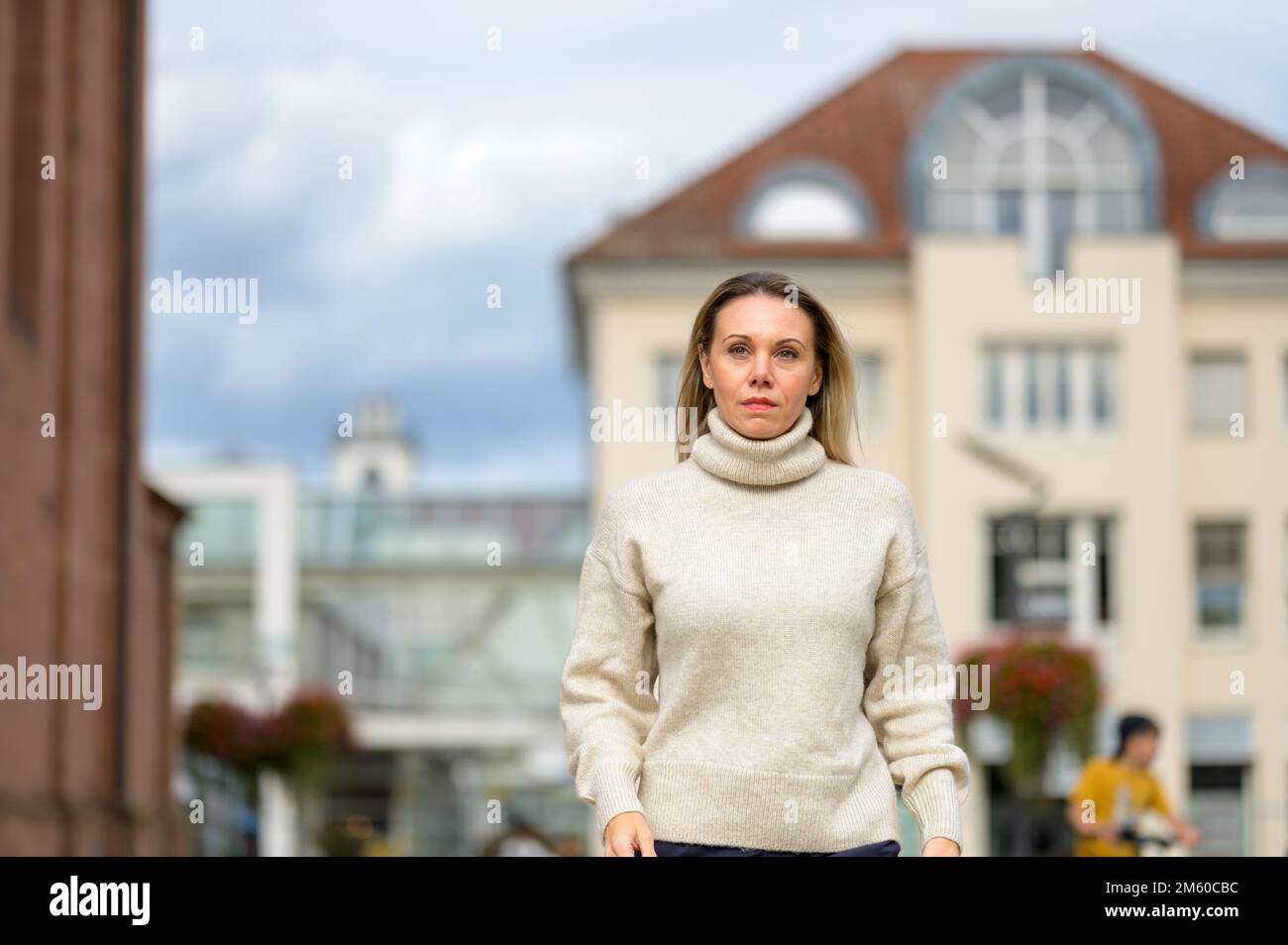 Bella donna bionda di mezza età che cammina attraverso un ambiente urbano con uno sguardo attento in lontananza Foto Stock