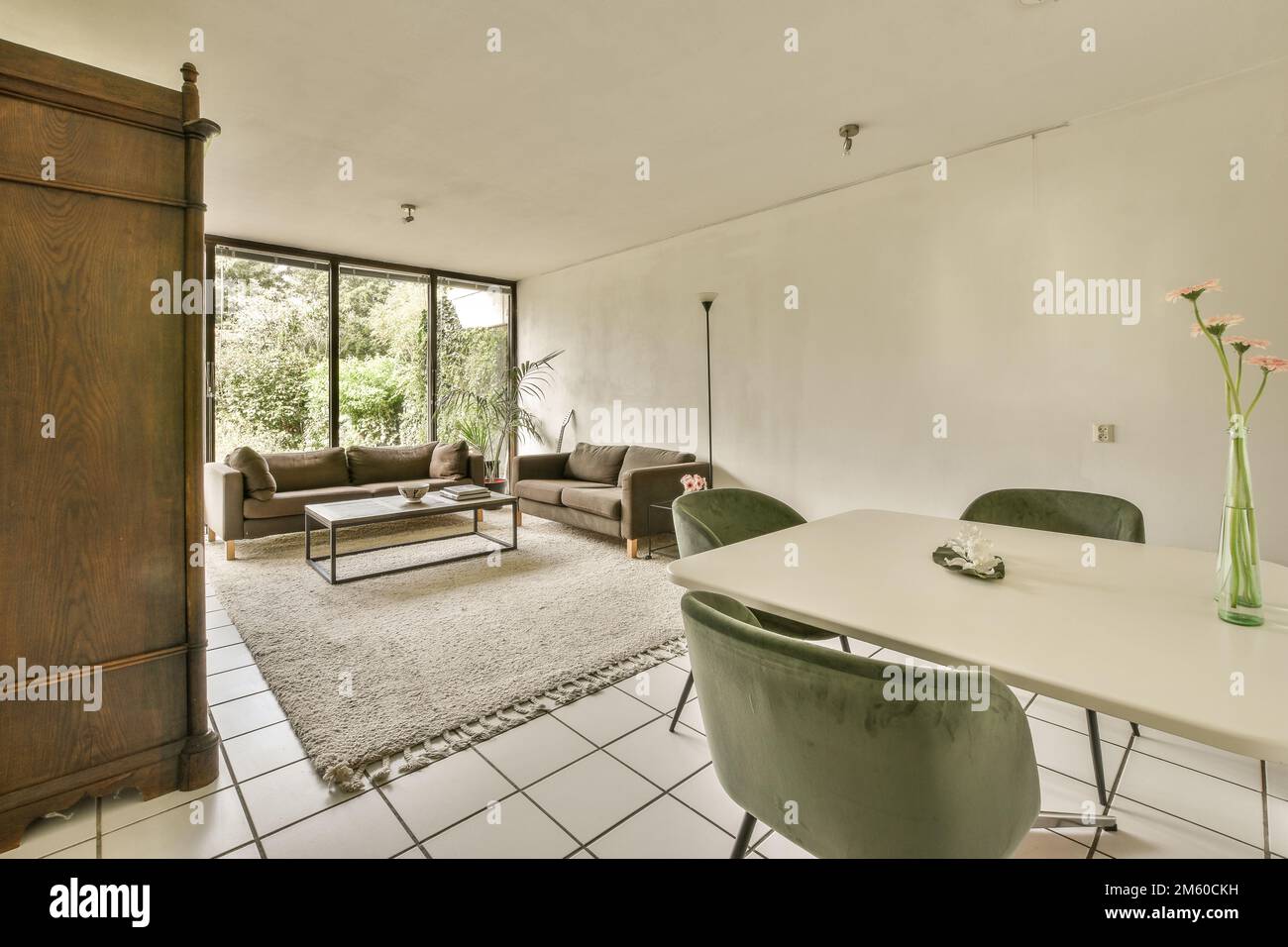 un soggiorno con pavimento in piastrelle bianche e grandi porte in legno che conducono al patio esterno, che e' aperto Foto Stock