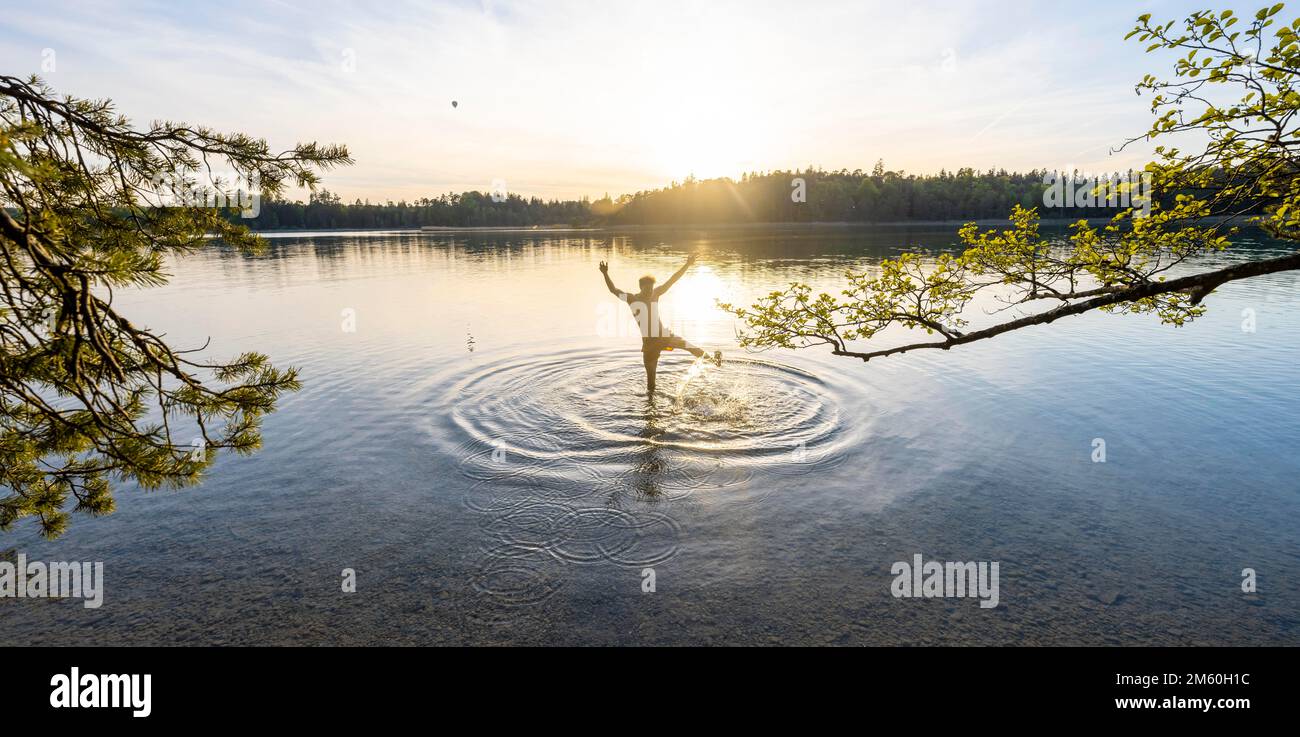 Giovane uomo che si stende le braccia in aria, bagno nel lago, spruzzi d'acqua, Fohnsee, Osterseen, vicino Iffeldorf, Baviera, Germania Foto Stock