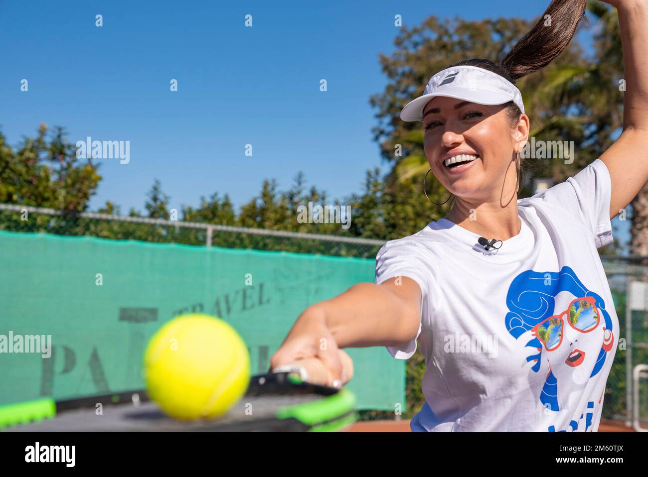 Donna allegra con racchetta da tennis e palla che tiene ponytail in campo Foto Stock