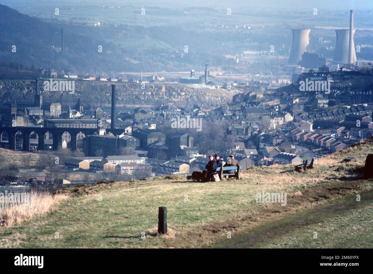 Uomini seduti su una panchina che domina la valle industriale nel 1983, Greetland, West Yorkshire Foto Stock