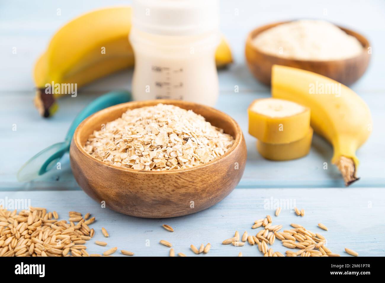 Latte in polvere e farinata d'avena, mix di banane, latte per bambini, succhietto, biberon, cucchiaio su sfondo di legno blu. Vista laterale, messa a fuoco selettiva Foto Stock