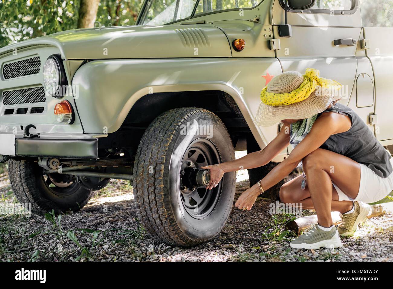 una donna avventurosa che indossa un cappello e una sciarpa, controlla le condizioni della ruota del suo veicolo fuoristrada durante una pausa. concetto di natura Foto Stock