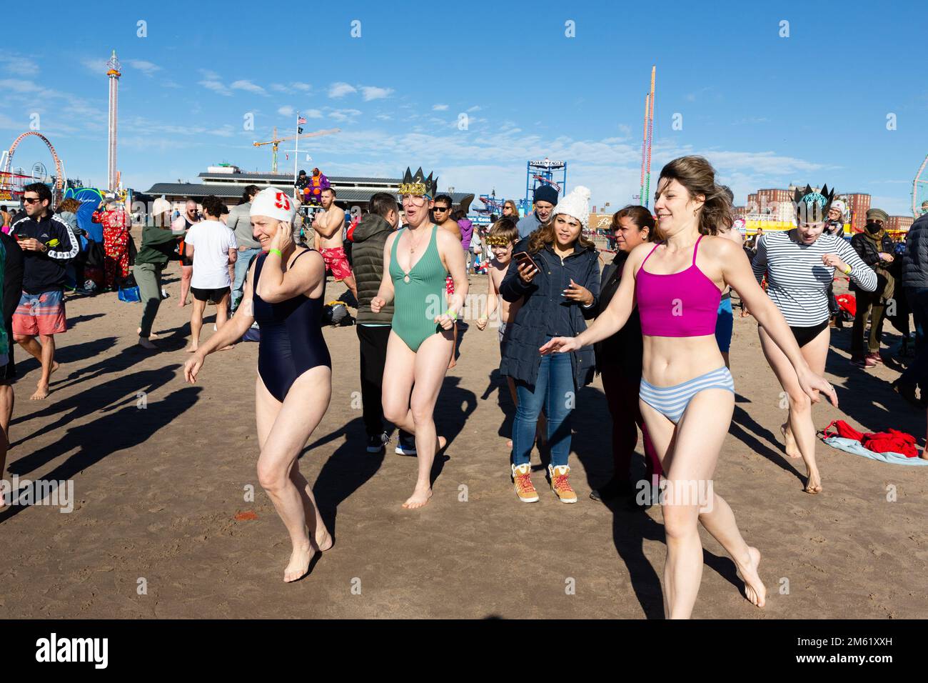 Brooklyn, New York, Stati Uniti. 1st Jan, 2023. Migliaia di bagnanti e spettatori si sono esibiti in un soleggiato e caldo Capodanno per l'annuale Polar Bear Plunge a Coney Island, sponsorizzato dall'Alliance for Coney Island. gruppo di donne corrono torreggi l'acqua. Mentre correvano, ho sentito dire "perché sto facendo questo?" Credit: Ed Lefkowicz/Alamy Live News Foto Stock