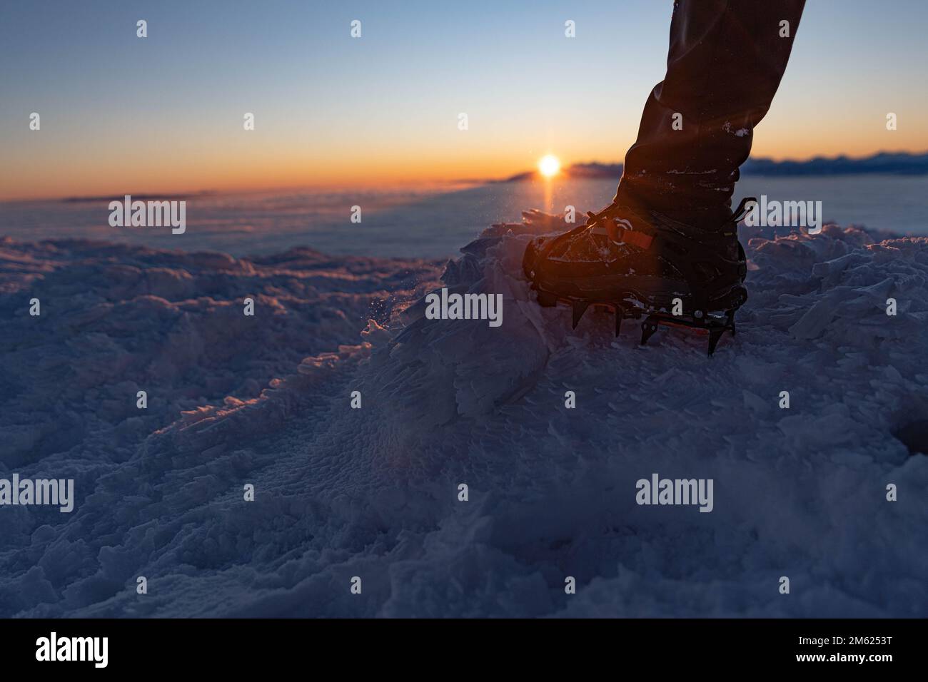 L'uomo sale una cima di montagna in inverno durante l'alba. Una scarpa con punte - ramponi. Foto Stock