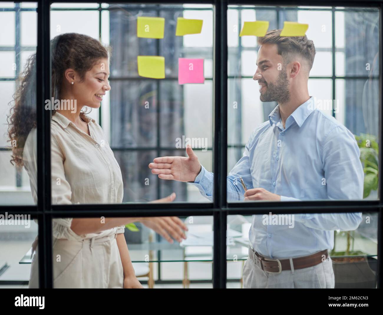 Professionisti creativi che si levano in piedi e discutono in ufficio dietro una parete di vetro con note appiccicose Foto Stock