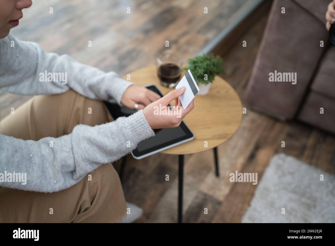 Una donna che acquista online hold carta di credito e tablet digitale mano di giovane donna adulta prendere la decisione di acquisto online mentre si siede a casa re Foto Stock