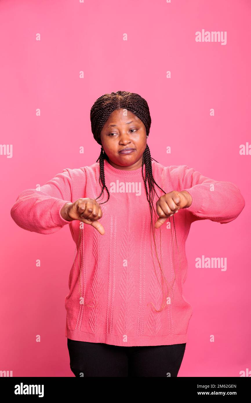 Donna insoddisfatta insoddisfatta che mostra un gesto dissimile sulla fotocamera in studio, gestendo il segno di disaccordo con le dita. Persona dispiaciuta che esprime disapprovazione e delusione, facendo simbolo di dispiacere. Foto Stock