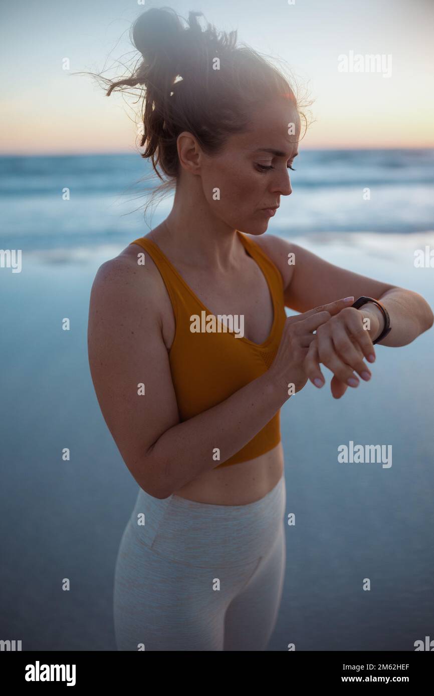 adatta la donna sportiva in abiti sportivi con il fitness tracker in spiaggia la sera. Foto Stock