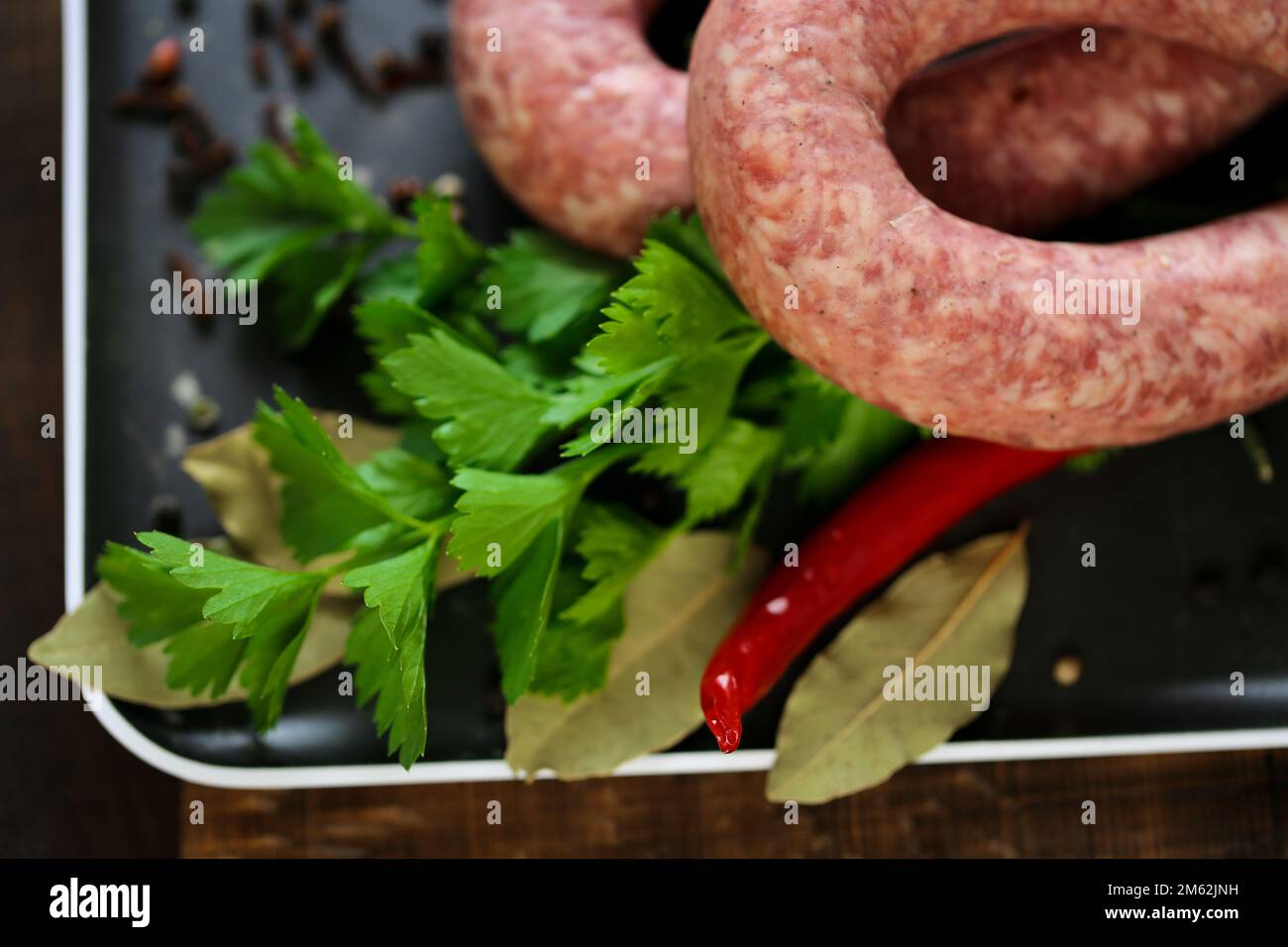 anelli di salsiccia, prezzemolo fresco, peperoncino rosso in un piatto nero su un tavolo di legno scuro. appetitosi prodotti di carne con erbe e verdure Foto Stock
