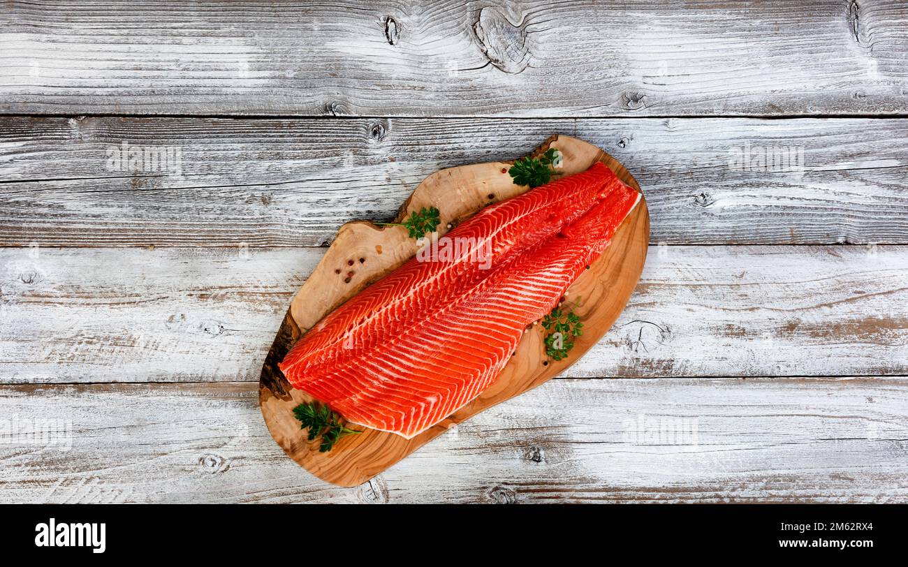 Filetto di trota di salmone, lato pelle in giù, su tavola di legno di ulivo con sfondo bianco rustico tavolo di legno Foto Stock