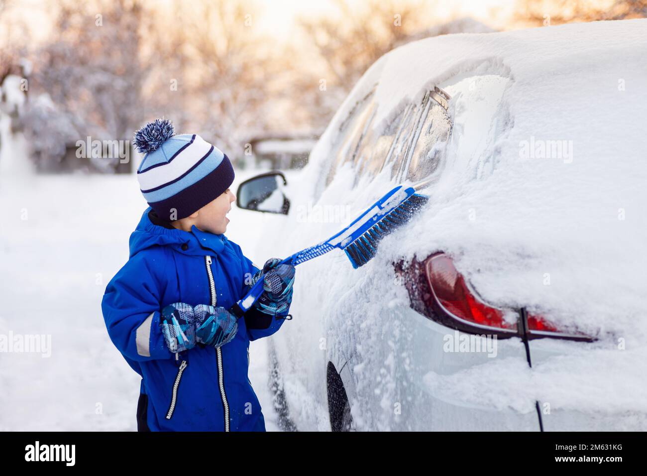 bambino che aiuta a pulire la neve dalla macchina dei padri Foto Stock