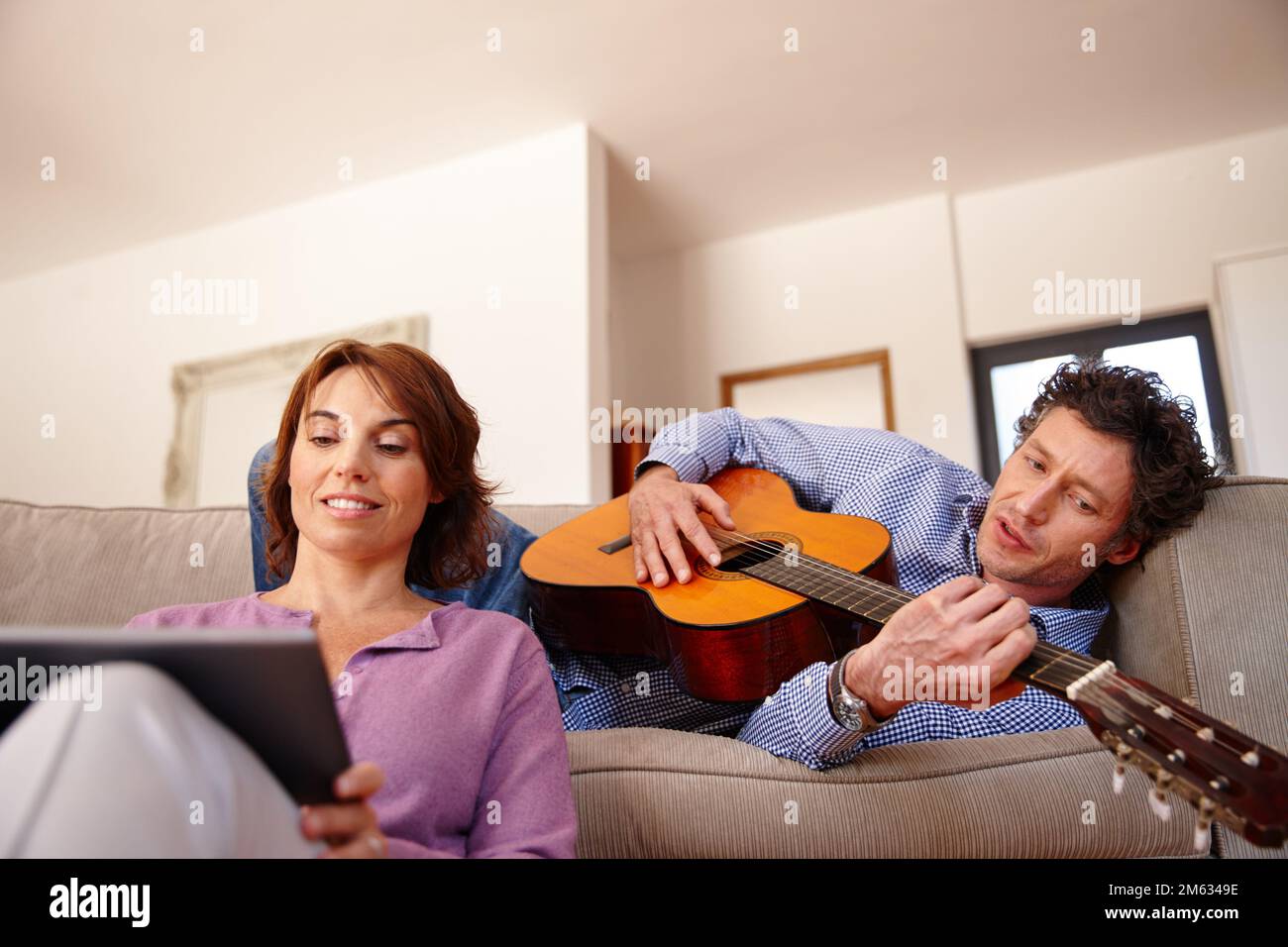 Lezioni di chitarra online. una donna che usa un tablet digitale mentre suo marito suona la chitarra. Foto Stock