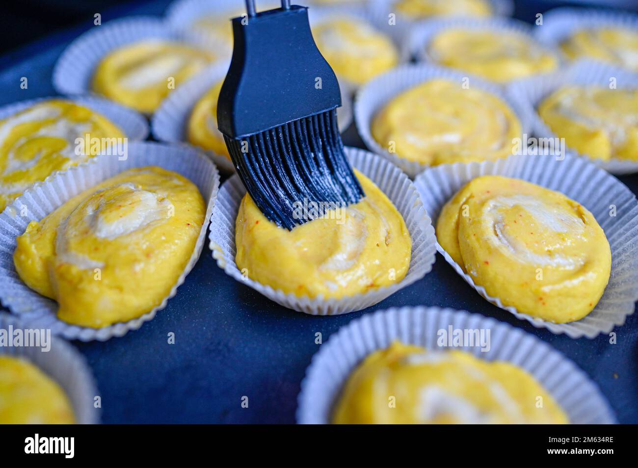 spazzolare l'uovo su ciambelle di zafferano gialle in cucina Foto Stock